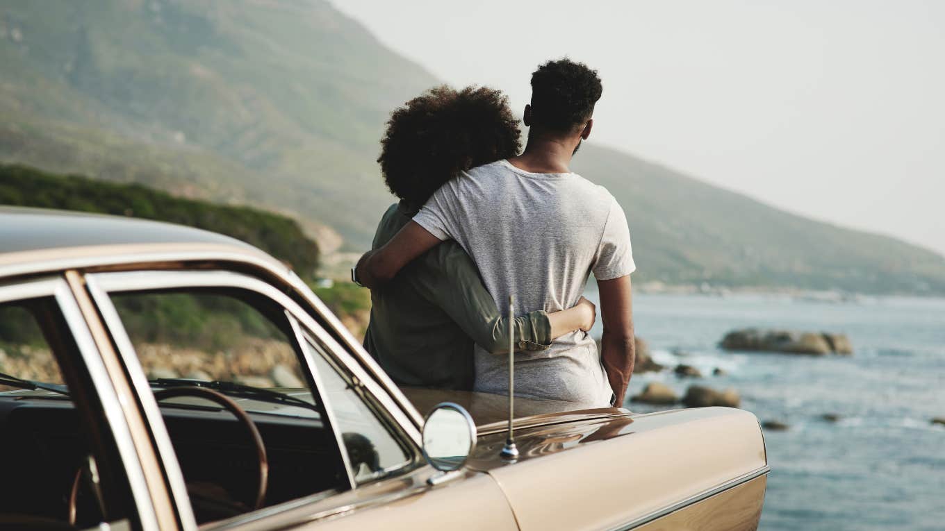 Couple sitting on the hood of car, looking at water