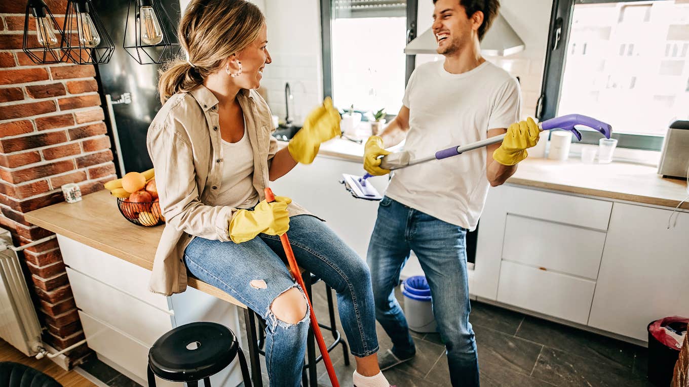 Couple in the kitchen cleaning, playing band with the cleaning tools