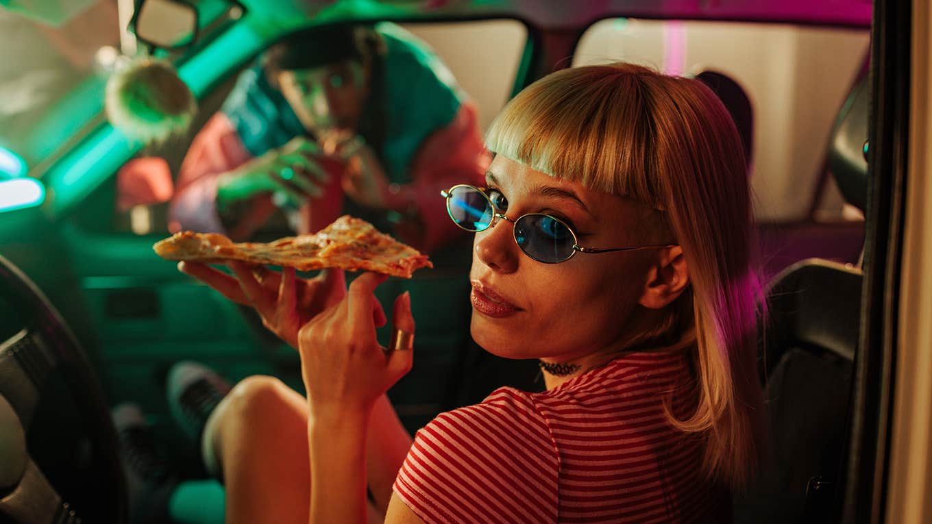 fashionable woman sitting in the car with pizza and her boyfriend looking through the passenger window
