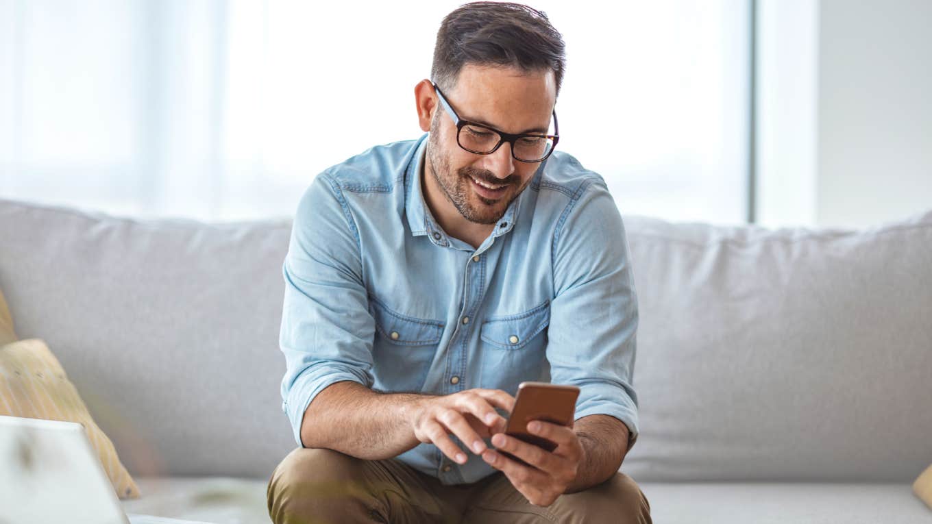 Man smiling while reading his phone. 