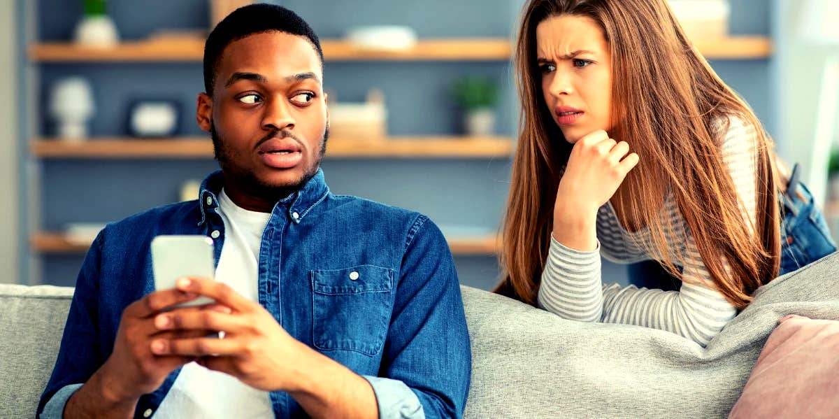 15 Red Flags In Men You Don't Want To Miss woman looking over boyfriend's shoulder while he's on his phone