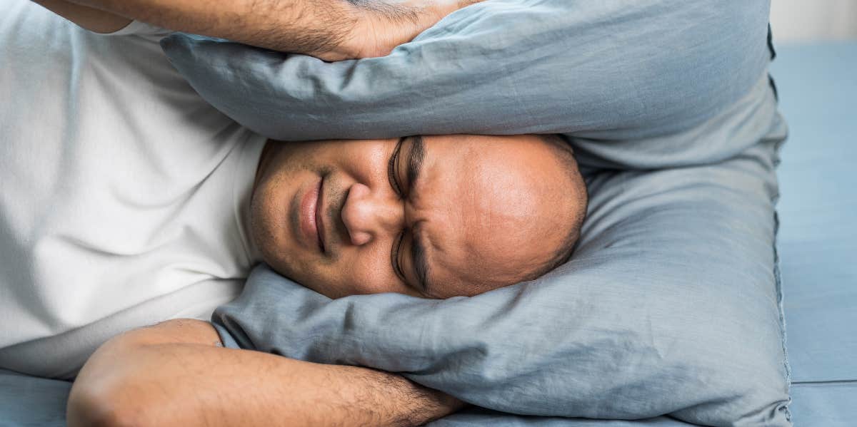 A man drowning out noise with a pillow