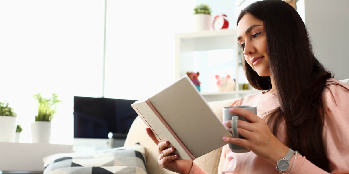 Woman reading while sitting on sofa with a cup in her hand