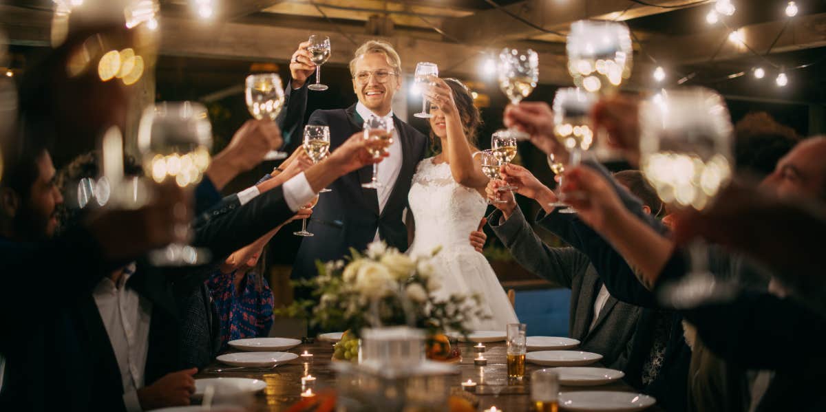 Bride and Groom Plan ‘Lavish’ Wedding They Can’t Afford — Beg Guests To Donate Money & Labor bride and groom celebrating wedding at reception with toast