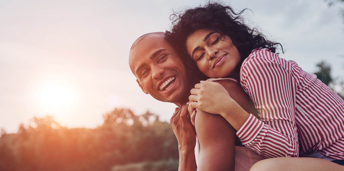 young and happy couple embracing and smiling while sitting on the pier near the lake