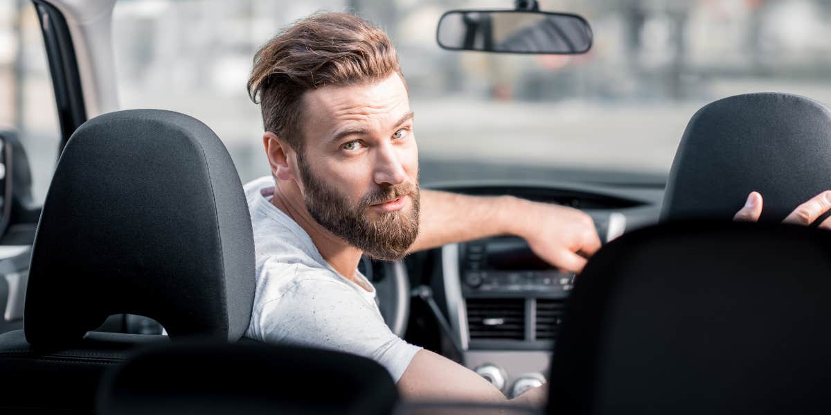 A guy looking back from the driver's seat of a car