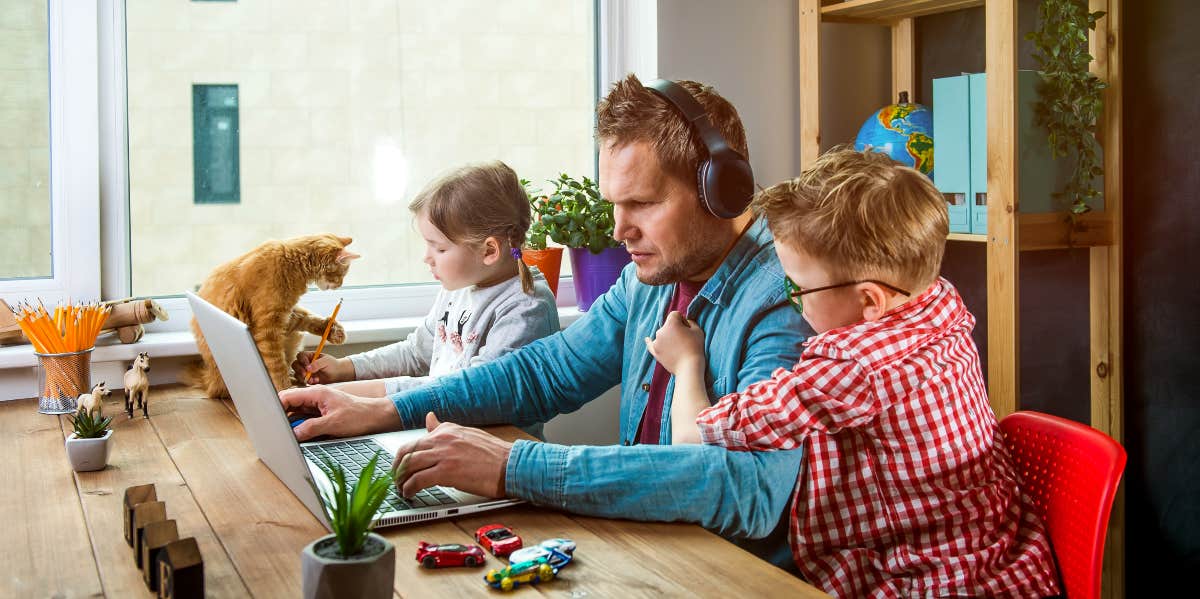 man working on laptop while children play around him