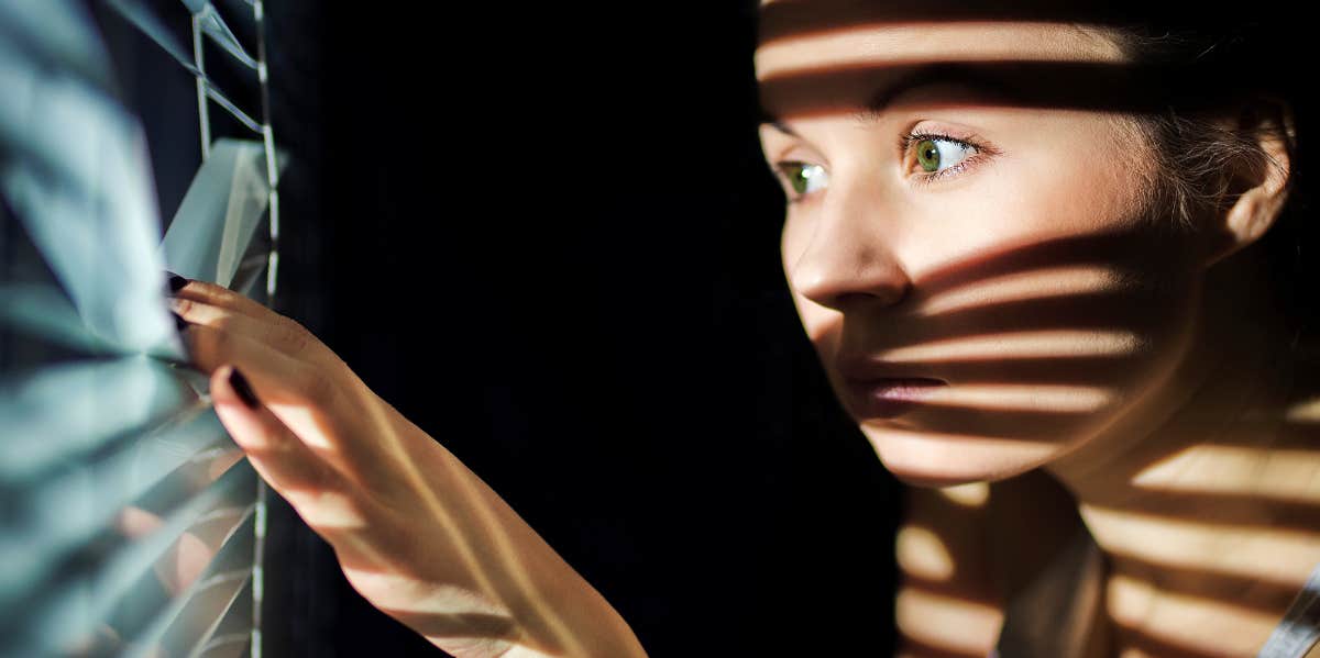 Woman looking through blinds at her neighbor