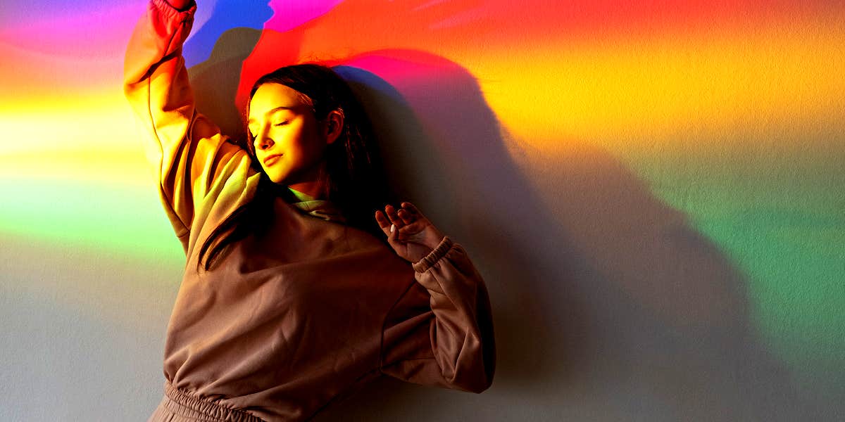 woman standing against a wall, a rainbow over her body