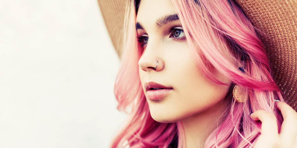 woman with pink hair and hat, looking slightly away