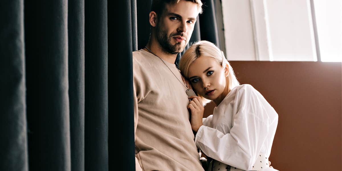 Signs your relationship is a power struggle Brunette man with short beard and sweatshirt hugging well-dressed bleached blonde in fancy clothes - both looking serious
