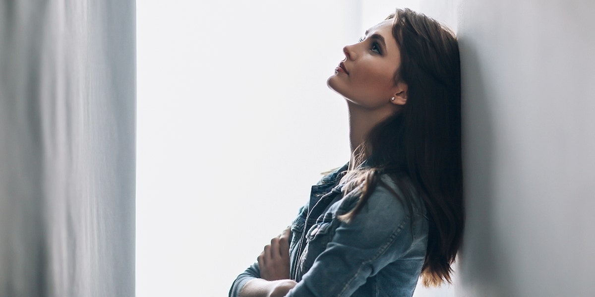 Almost 50% Of Women Regret This Part Of Their Relationship woman looking frustrated leaning up against white wall