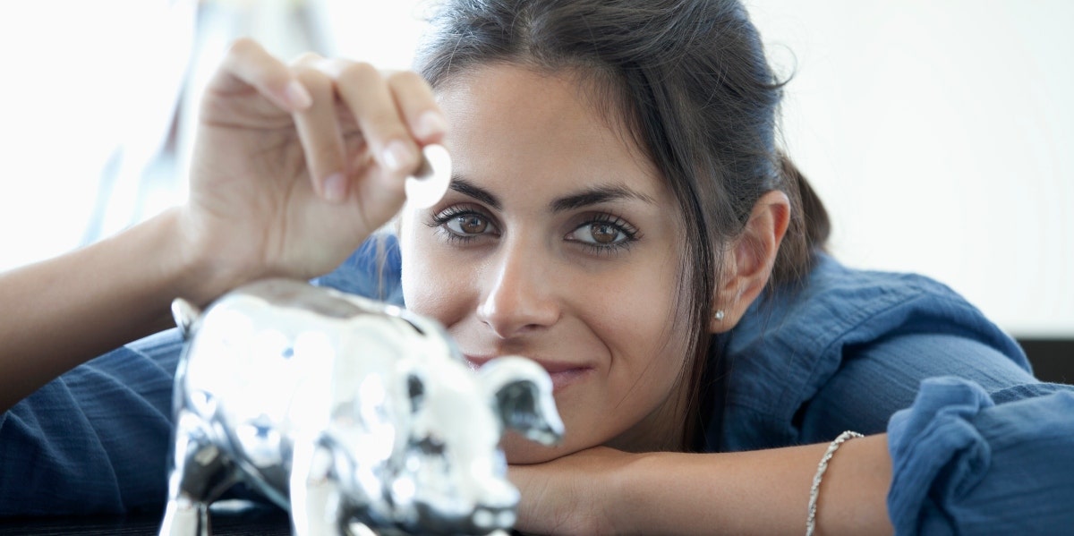 smiling woman putting coins in a piggy bank