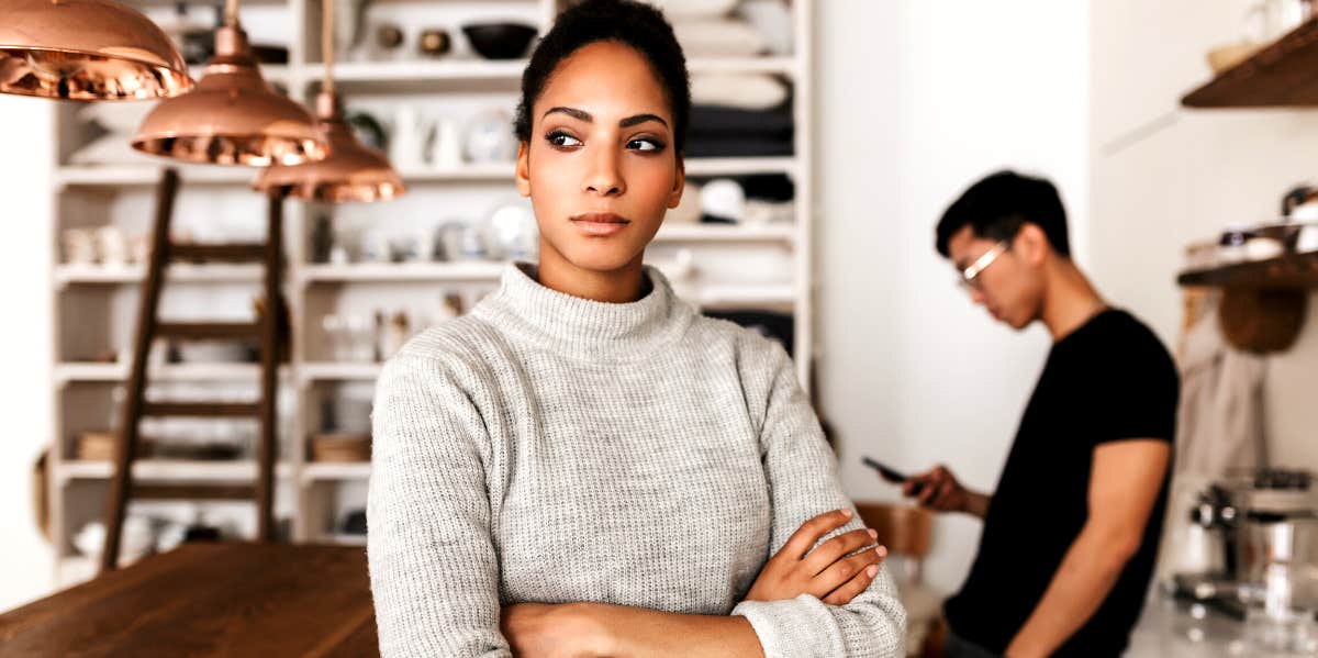 woman with arms folded feeling resentment while man looks at his phone