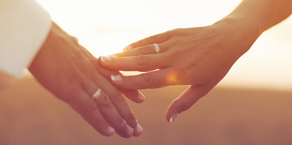 The Surprising Reason We Don't Always Wear Our Wedding Rings couple touching hands in sunset