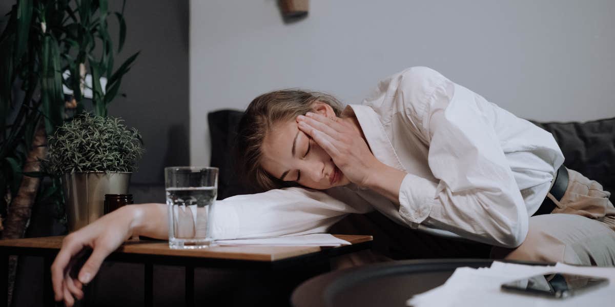 tired woman laying down on desk next to glass of water