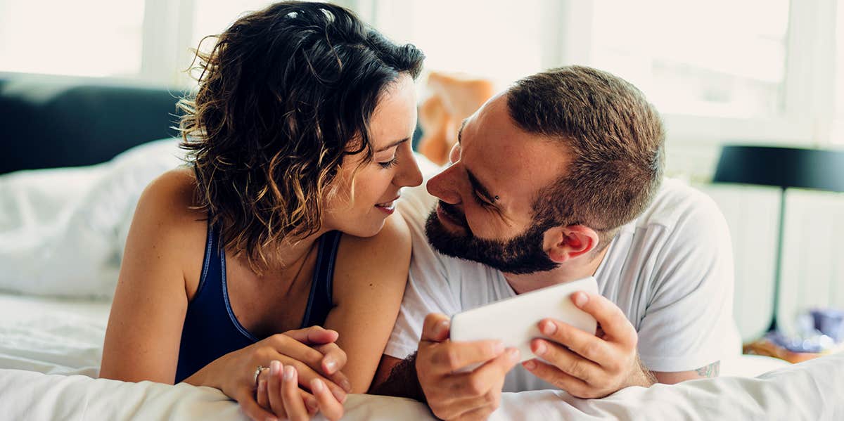 couple laying on bed guy holding phone