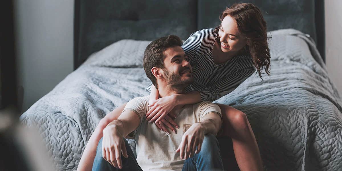 couple sitting in front of bed smiling at each other