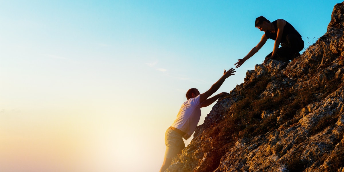 man helping another climb up a rock