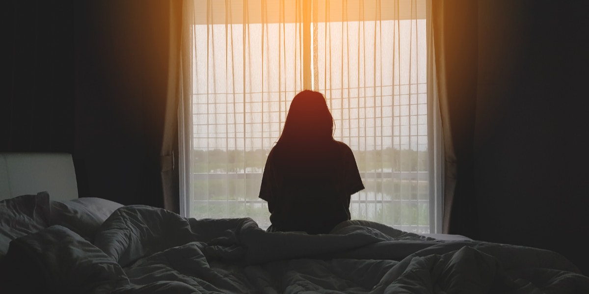 woman sitting on bed and looking out a window