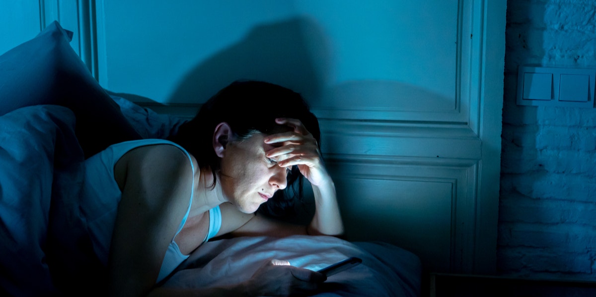 man in bed looking at phone nighttime