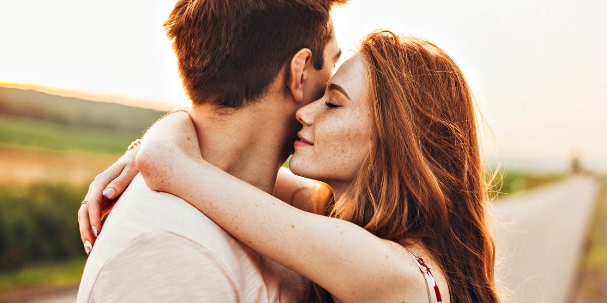 Redheaded woman hugging man who is turning away, country road in the evening