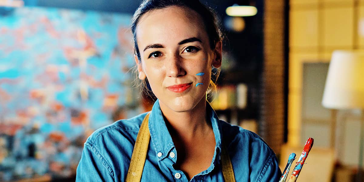 woman smiling confidently in front of a painting, wearing an apron