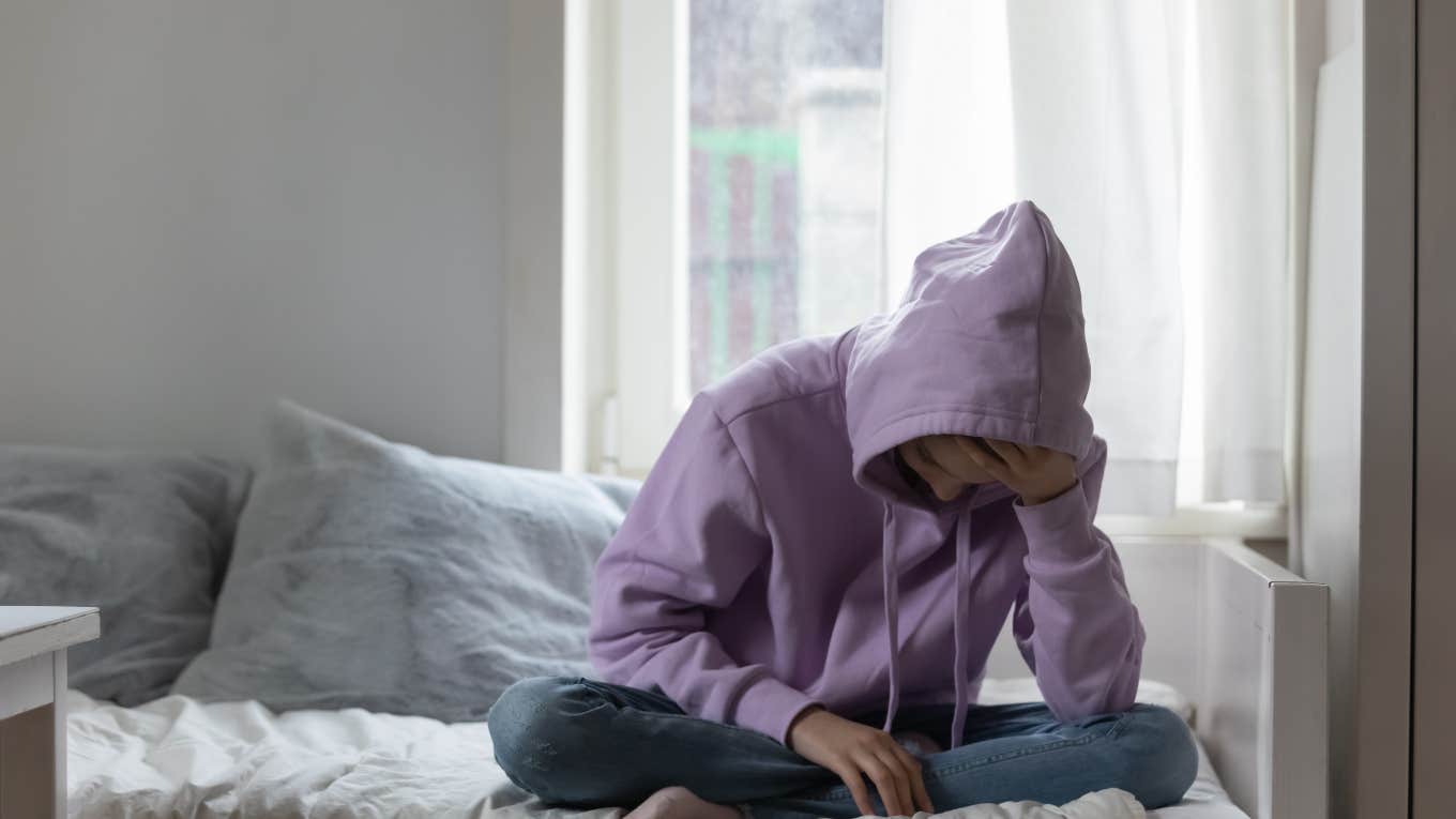 sad young person sitting on bed in hoodie