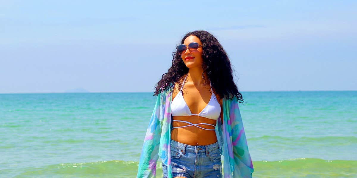 joyful woman in shorts and bikini top in front of a Caribbean beach