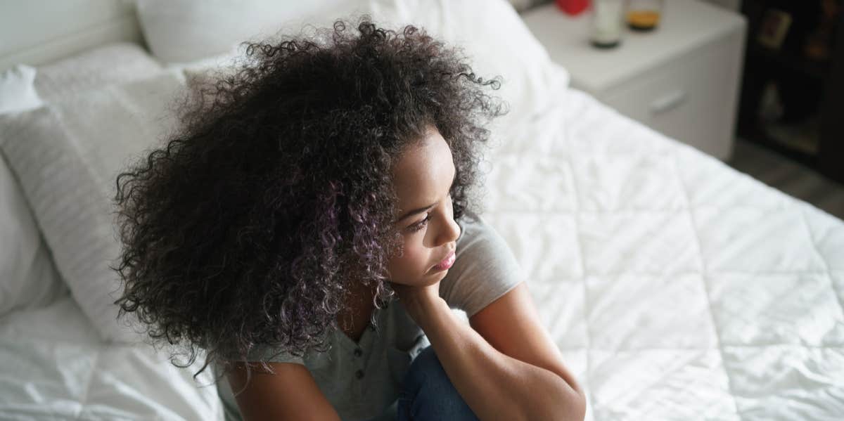 He Raped Me, But I Went Out With Him Again. Here's Why. woman on bed with hand on face