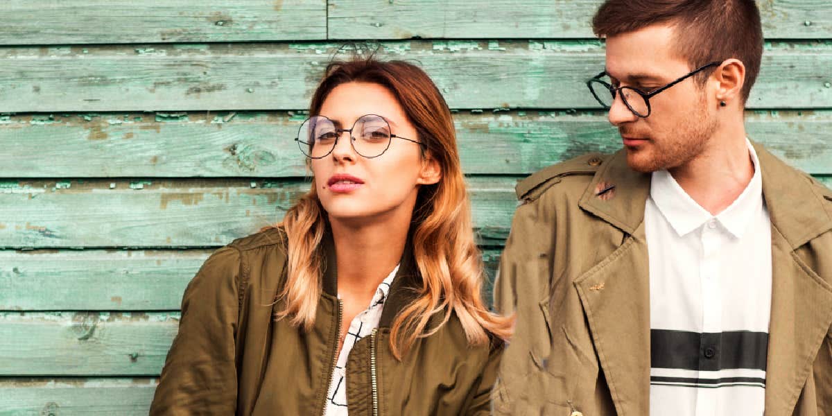 man and woman standing against a wooden wall painted green