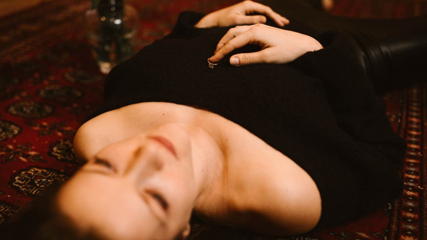 Woman laying on the floor of her bedroom with her ring on her chest contemplating her relationship