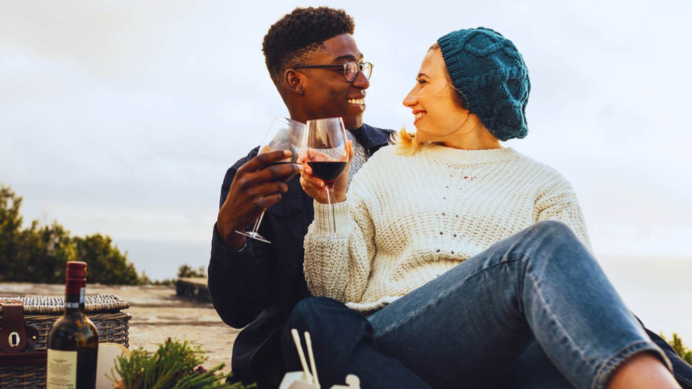 woman sitting on man's lap enjoying wine on picnic date