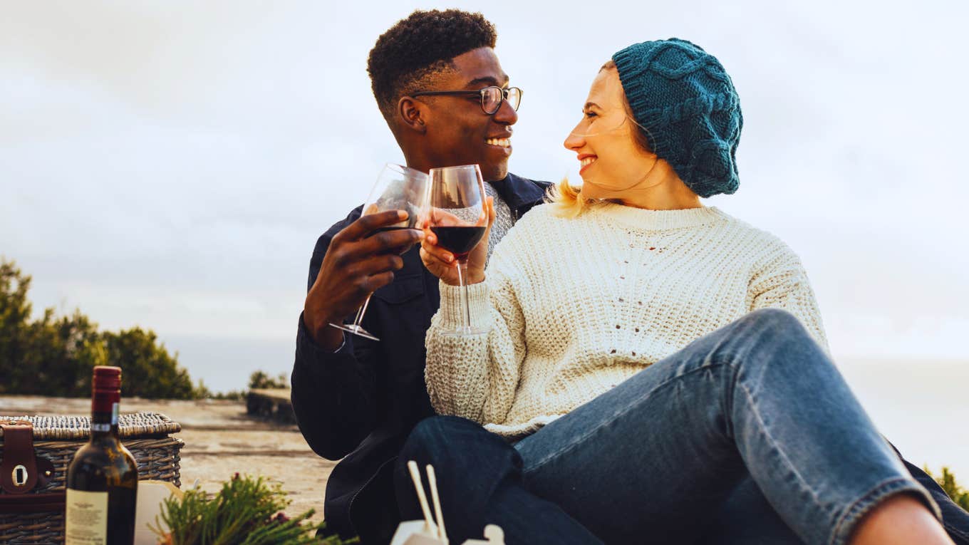 3 Tiny Hints A Guy Is Falling Insanely In Love With You woman sitting on man's lap enjoying wine on picnic date