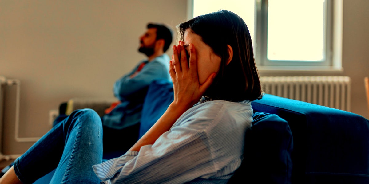 woman with hands over face on couch next to man