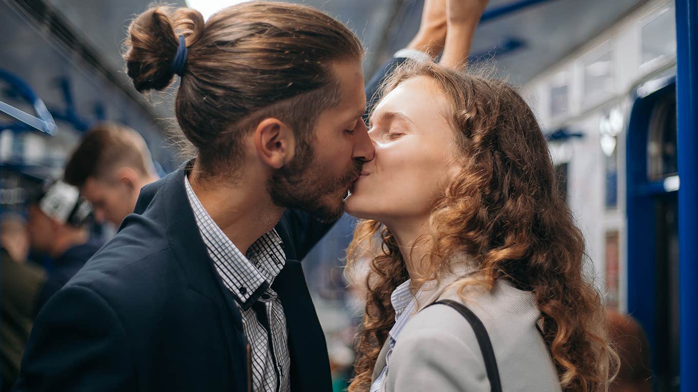kissing couple standing on a subway train.