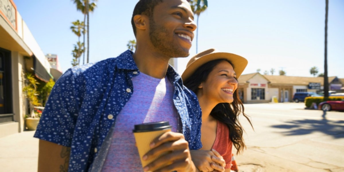 man and woman smiling holding coffee walking