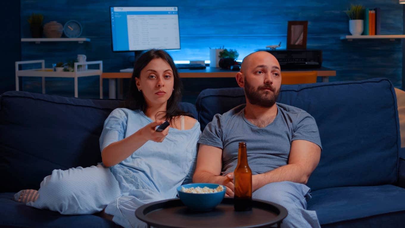 Young couple spending evening together dressed in pajamas arguing for remote control