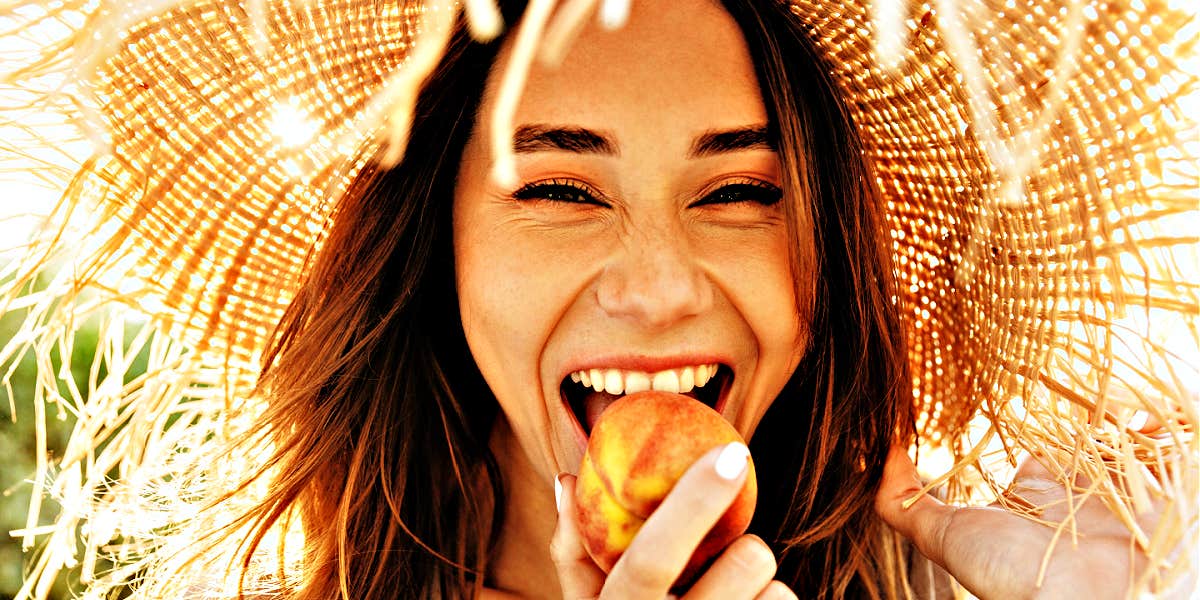 woman in straw hat joyfully eats a peach