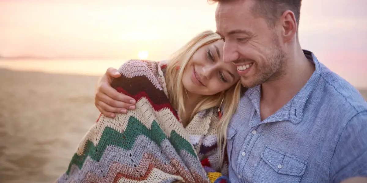 Woman smiling laying on man's shoulder as the sun sets