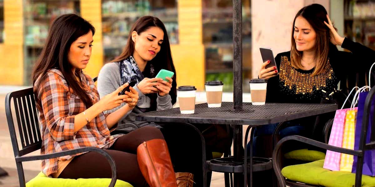 group of friends sitting at a table looking at their phones instead of talking to each other