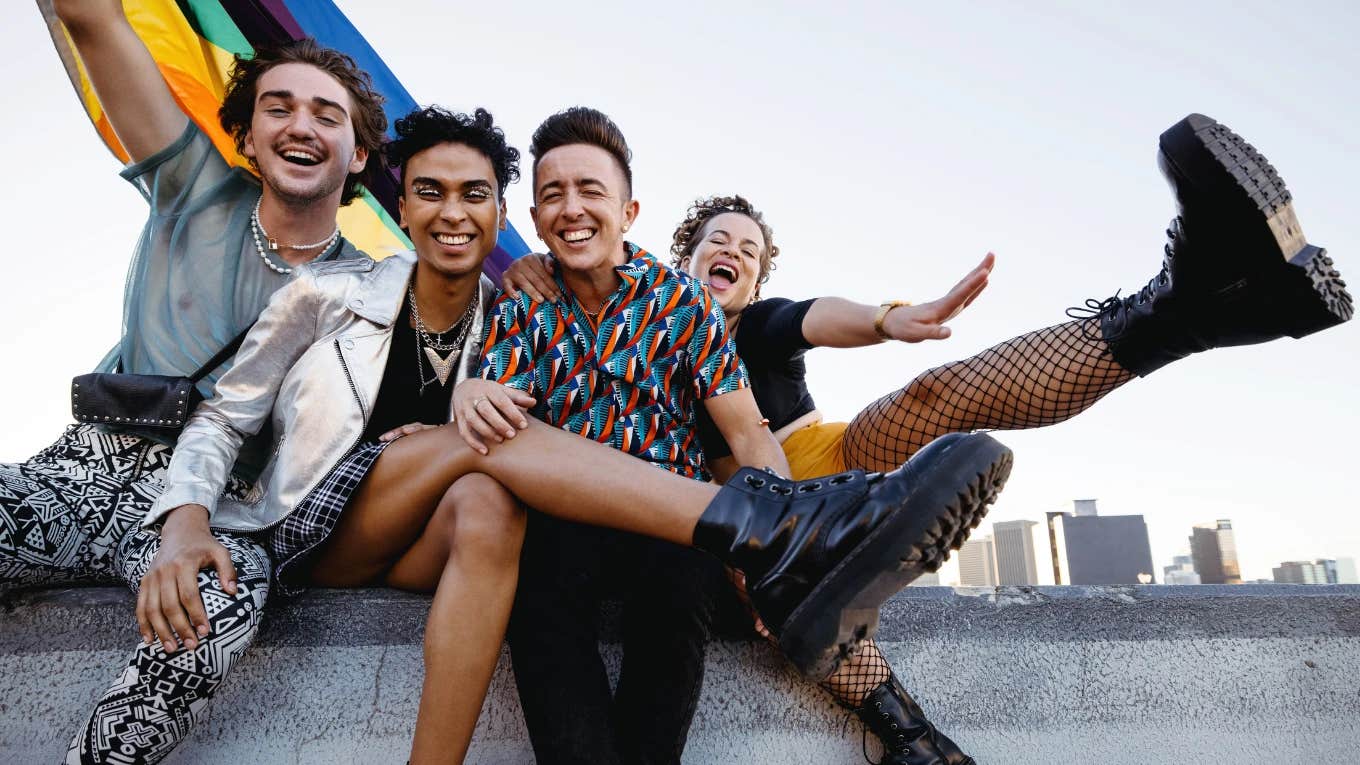 Four friends smiling and hugging each other with a pride flag