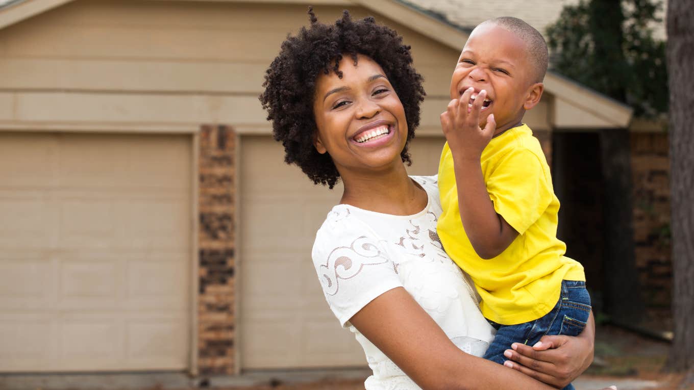 mother holding her son standing in front of their garage