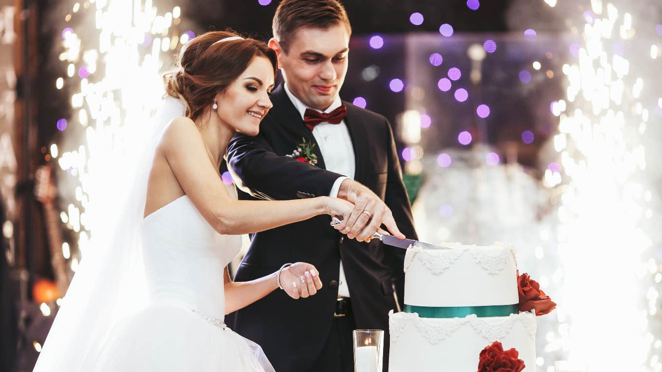 bride and groom cutting a white cake with red flowers