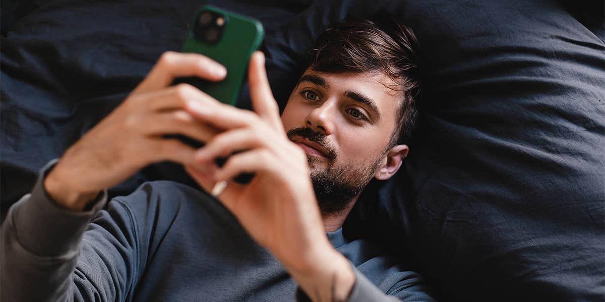 man laying in bed looking at phone