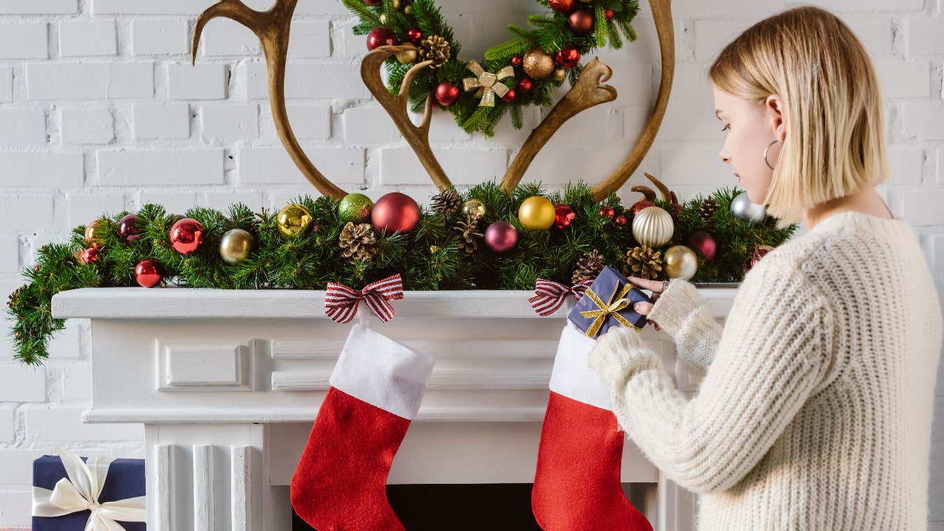 woman filling christmas stockings over fireplace