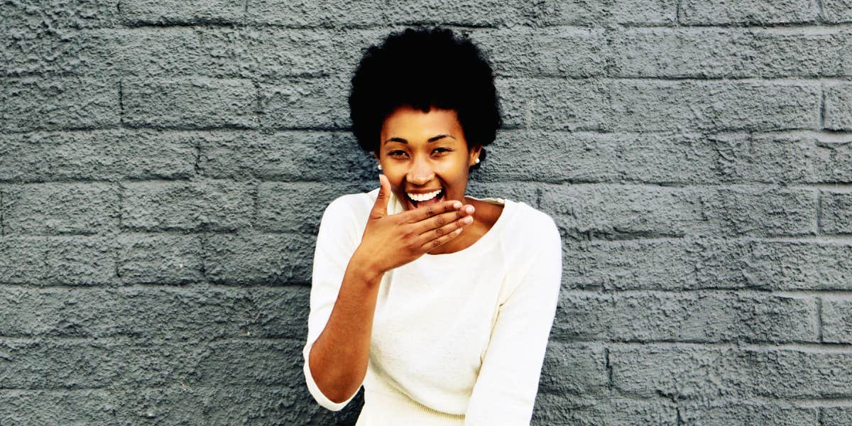 Black woman laughing in front of a brick wall