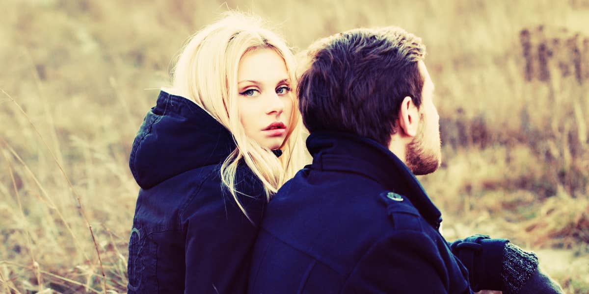 couple in a field, blonde woman looks right at camera while man looks away