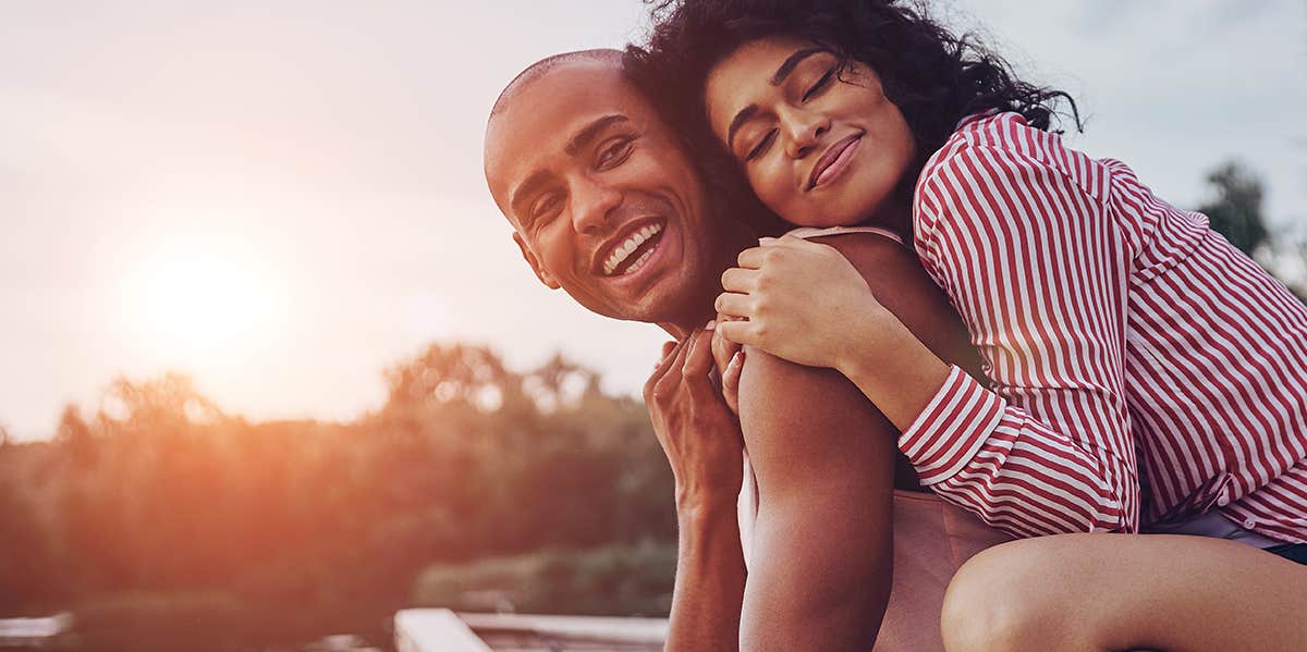 woman clutching husband's back in sunset