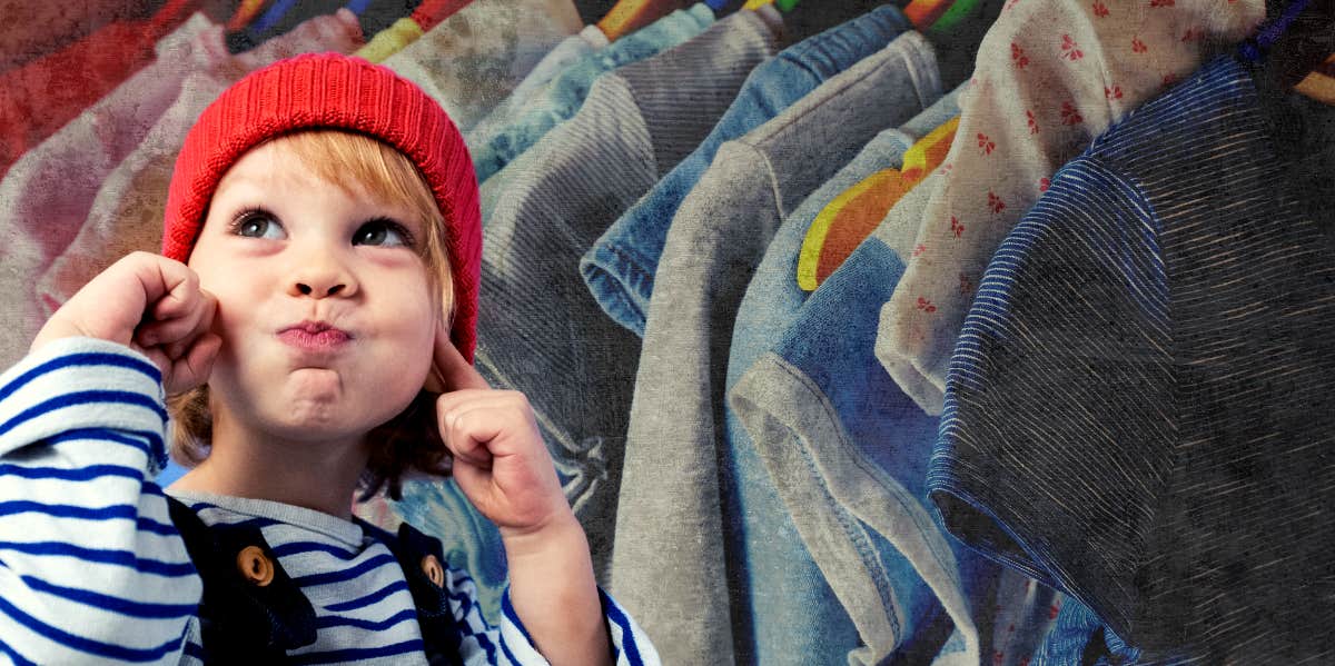 A young child is next to a rack of clothing.